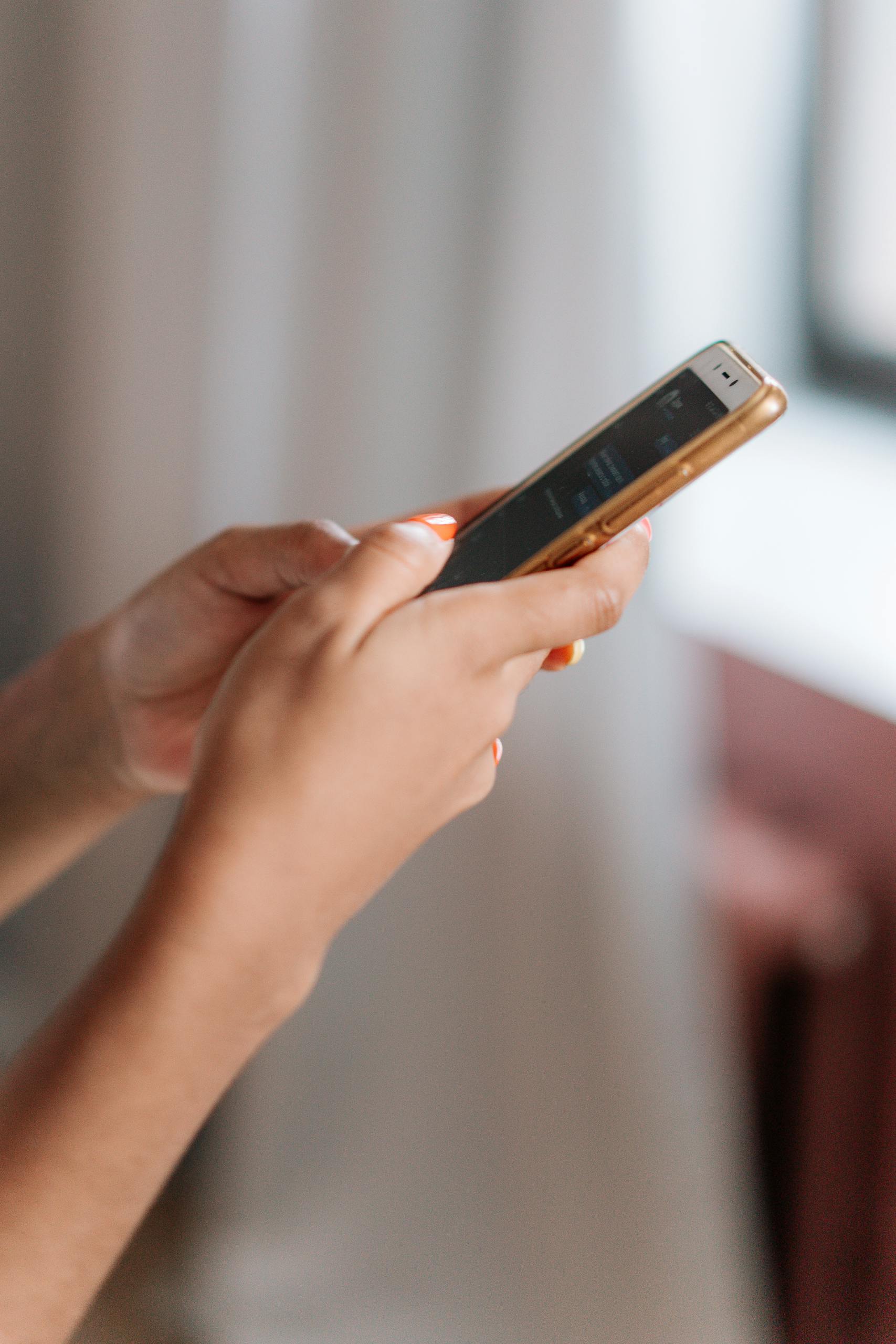 A side view close-up of a person's hands using a smartphone with a blurred background.